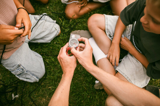 Directly above shot of instructor demonstrating navigation skills with compass to children sitting in circle at summer c