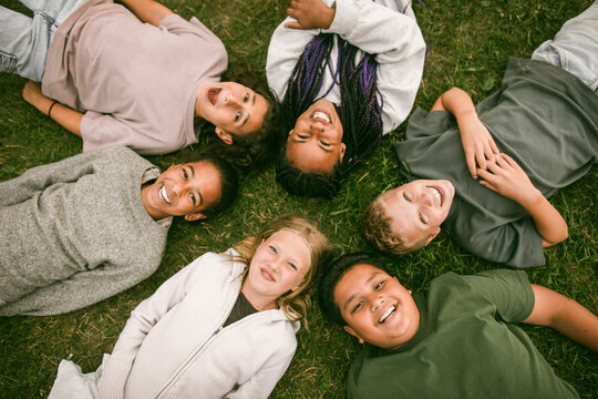 Directly above shot of happy children lying in circle on green grass at summer camp