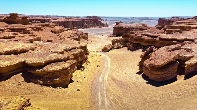 High angle view reveals a winding dirt trail cutting through the vast yardang landforms of Dahaidao in Xinjiang under clear blue sky.