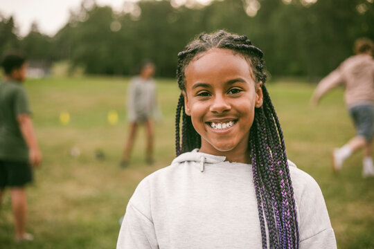 Portrait of smiling girl with long braids wearing gray hoodie at park
