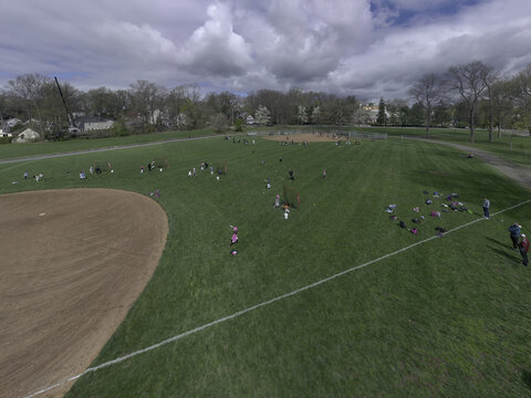 Aerial view of a baseball field in a park with players practicing on the grass and dirt infields, surrounded by trees under a cloudy sky in Summit, New Jersey, United States.