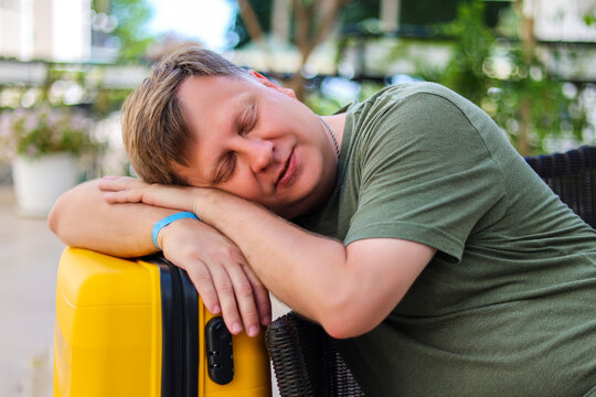 Tourist sleeping on suitcase in hotel lobby waiting for airport transfer, tired traveler rest, vacation end, luggage, journey concept.