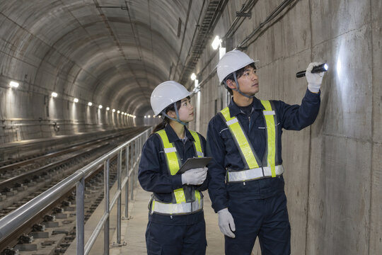 鉄道トンネルの保守通路で壁面を点検する二人の作業員