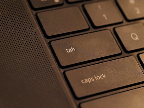 Macro close-up shot focusing on the tab and caps lock keys of a modern black laptop keyboard under warm lighting