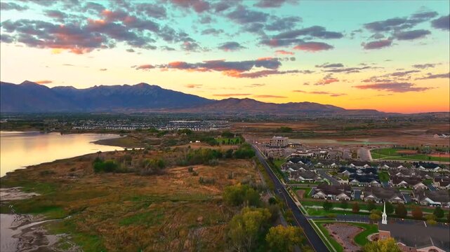 Aerial sunset view over a suburban neighborhood near a lake with distant mountain range horizon