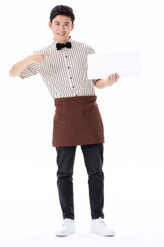 Smiling Asian waiter in uniform pointing at blank white sign board