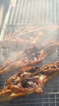 Slow motion of authentic Thai grilled chicken (Kai Yang) sizzling on charcoal grill.