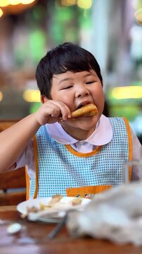Happy Asian boy eating delicious Thai grilled chicken drumstick, slow motion.