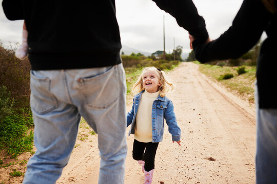 Little girl laughs while walking with parents on dirt path