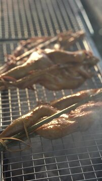 Slow motion of authentic Thai grilled chicken (Kai Yang) sizzling on charcoal grill.