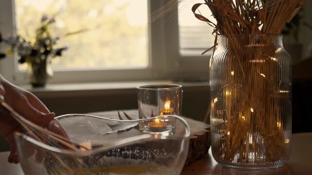 Whisking egg dough mixture in glass bowl in cozy kitchen with fairy lights