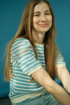 Young happy blonde woman with long healthy hair and blue eyes in striped top smiling at camera in studio on blue background