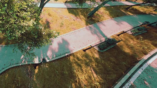 Curved walkways meander through a lush green park, bathed in warm sunlight. Shadows of trees dance on the path, creating a serene and inviting atmosphere for a pleasant stroll.