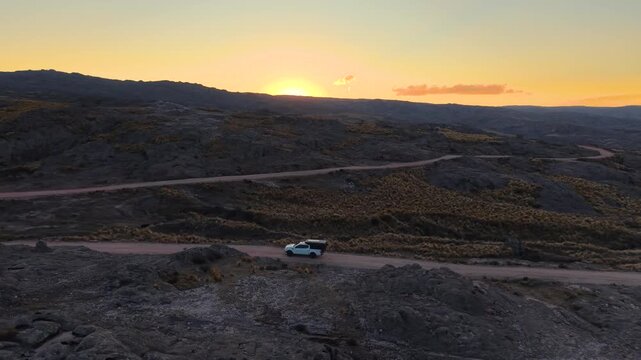 Drone view of offroad overland vehicle traveling through rugged mountain trail during golden hour in Altas Cumbres Cordoba