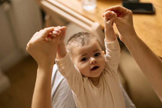 Baby holds hands up while adult gently lifts arms in warm indoor home moment