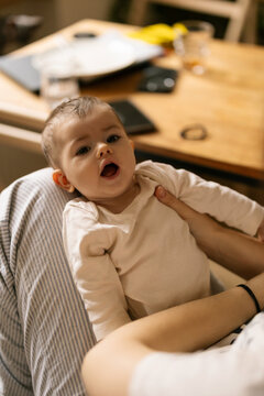 Baby looks up wide eyed while being held close in warm home setting