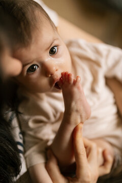 Baby looks up with wide eyes as adult holds foot gently in warm cozy indoor light