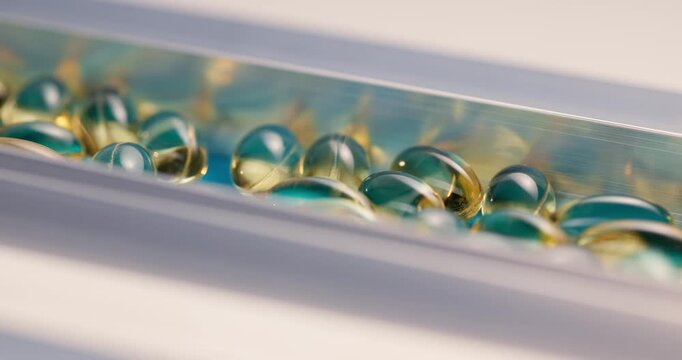 Golden translucent softgel capsules in metallic conveyor on pharmaceutical production line.