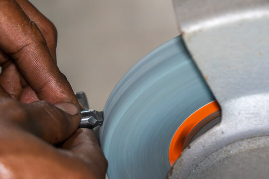 Machine operator manually regrinding a lathe cutting tool on an abrasive stone wheel