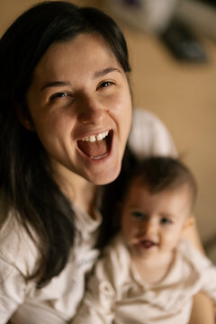 Happy mother laughs while holding baby in cozy home setting