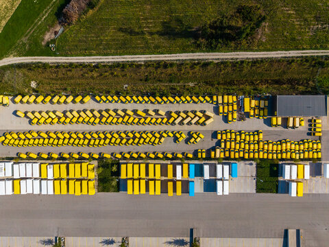 Aerial view of the Logistikzentrum Allhaming featuring rows of yellow delivery vans and white trailers parked in a large asphalt yard in Allhaming, Oberosterreich, Austria.