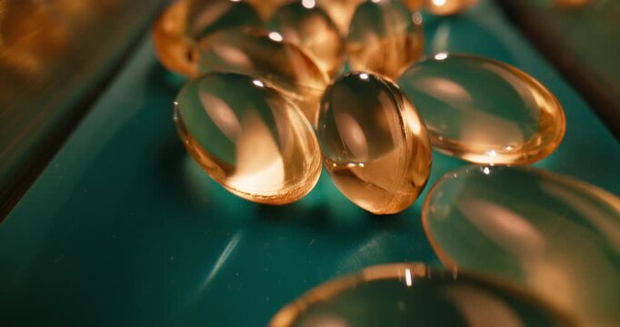 Slow motion probe closeup of gel capsules rolling on pharmaceutical conveyor with amber reflections in factory.