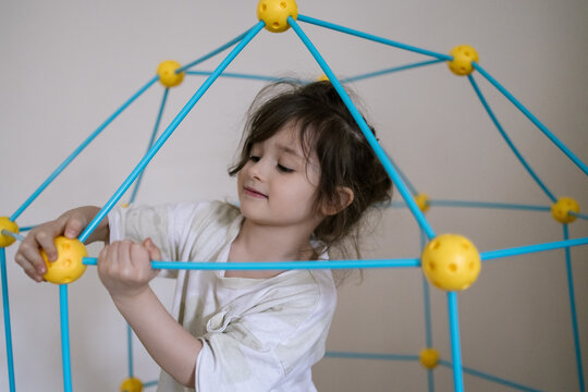 Young girl plays with colorful geometric toy inside cozy home space smiling naturally