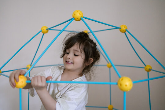 Young girl smiles while building colorful geometric structure with hands and joyful expression in bright room