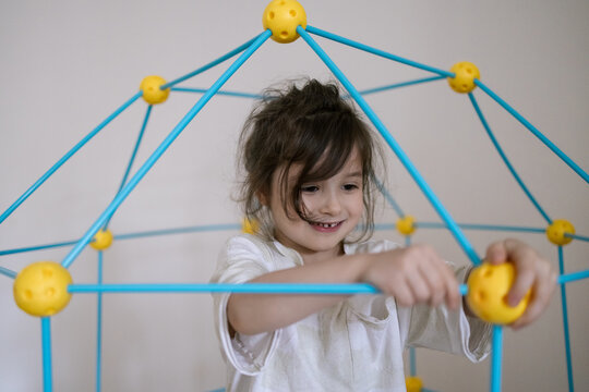 Young girl smiles while building colorful geometric toy structure indoors