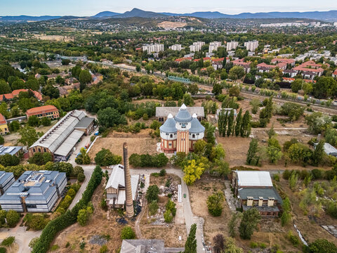 Aerial view of the restored air distillery and industrial buildings at the former Obuda Gasworks, surrounded by railway lines, trees and housing in Budapest, Hungary.