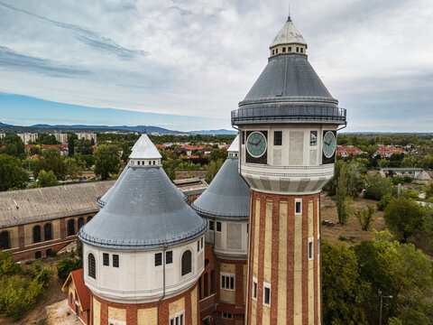 Aerial view of the restored historic towers of the former Obuda Gasworks above industrial buildings, trees and residential neighborhoods in Budapest, Hungary.