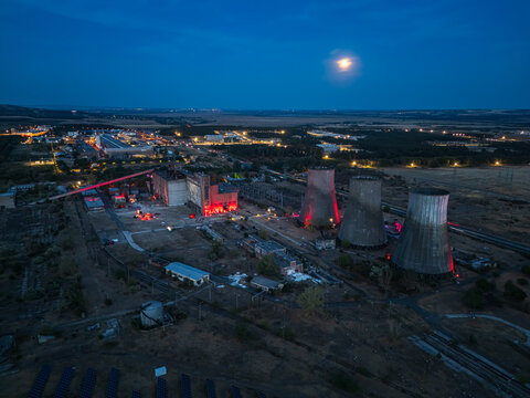 Aerial view of the former thermal power plant in Inota, Hungary, with illuminated cooling towers, industrial buildings and a moon over the site on a late summer evening.