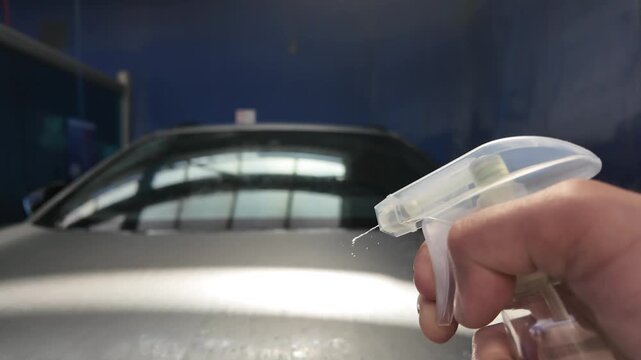 Man spraying auto chemical fluid from spray bottle on a car close-up, professional car wash and detailing service, cleaning vehicle glass with trigger sprayer, window cleaner.