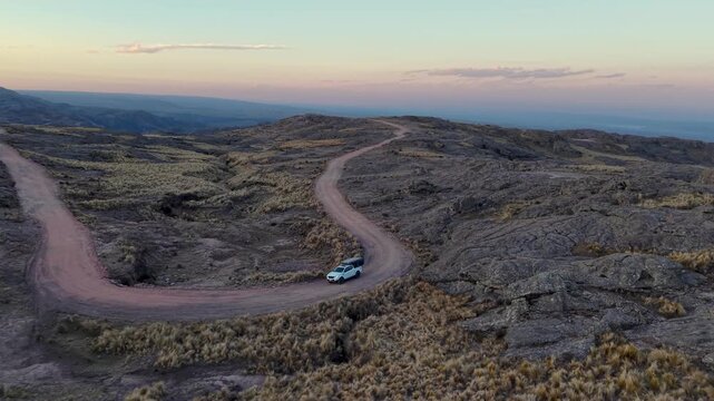 High angle drone shot following white 4x4 camper truck navigating hairpin turn on mountain dirt road at sunset
