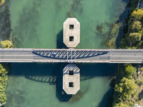 Aerial view of Ura e re e Bunes bridge crossing the turquoise Buna River with a car driving across and geometric shadows cast on the water in Shkoder, Qarku i Shkodres, Albania.