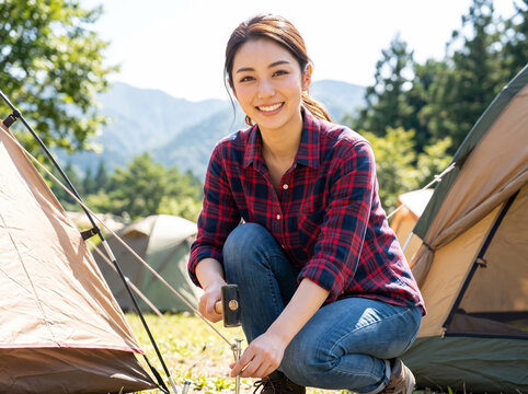 キャンプ場で笑顔でテントのペグ打ちをする女性