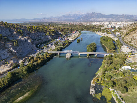 Aerial view of Ura e re e Bunes spanning the Buna River with lush riverbanks, surrounding mountains, and the city of Shkoder in the background, Shkoder, Qarku i Shkodres, Albania.