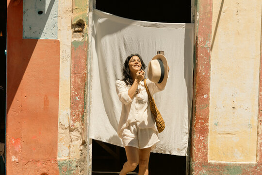 Empowered Woman Over 50 Traveling and Enjoying an Active Lifestyle, Wearing White Summer Fashion and Sun Hat Against Colorful Historic Architecture on a Sunny Vacation