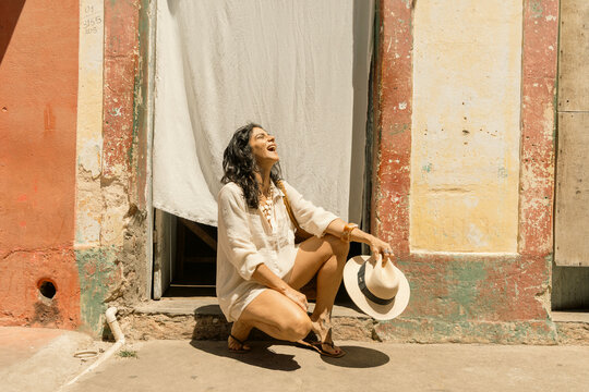 Empowered Woman Over 50 Traveling and Enjoying an Active Lifestyle, Wearing White Summer Fashion and Sun Hat Against Colorful Historic Architecture on a Sunny Vacation