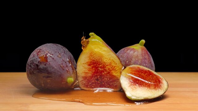 Sweet honey syrup pours and drips on ripe cut figs inside studio during detailed macro slow motion flight. Cinematic organic food video footage provides rich dark backdrop for design element.