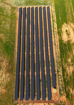 Aerial view of a large solar panel array set within a rural field, showcasing rows of photovoltaic modules capturing sunlight for renewable energy production in Ladismith, Western Cape, South Africa.