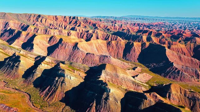 High angle shot of colorful danxia landform in Xinjiang during daytime, showing unique geological rock formations under blue sky.