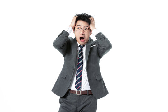 Stressed Asian businessman in suit holding head and shouting on white background