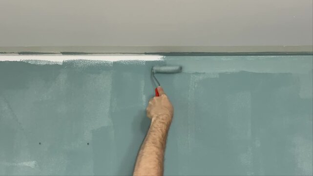 Hand rolling blue paint along ceiling line from right to left with roller