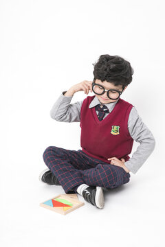 Thoughtful Schoolboy in Glasses Sitting with Colorful Tangram Puzzle