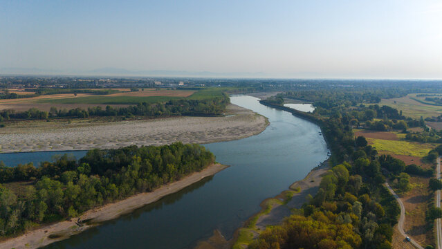 Aerial view of the Po River with low water levels due to drought, exposing sandy riverbeds and sediments surrounded by lush vegetation in Castelvetro Piacentino, Emilia-Romagna, Italy.