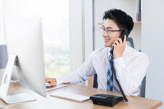 Smiling Asian Businessman Talking on Phone at Office Desk