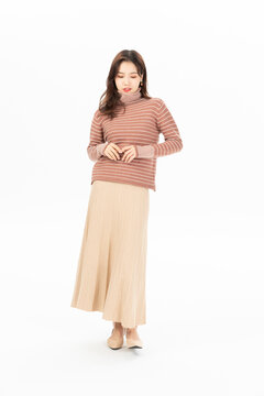 Young Asian woman in striped sweater and long beige skirt posing in a studio