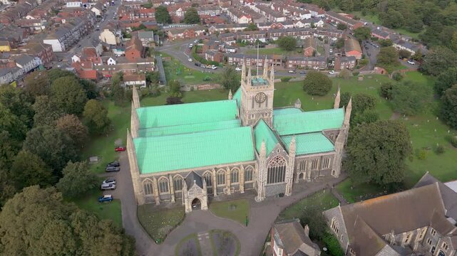 A close drone orbit movement of the historic 12th Century flint built Minster or parish Church in Great Yarmouth, Norfolk, UK surrounded by houses and other buildings