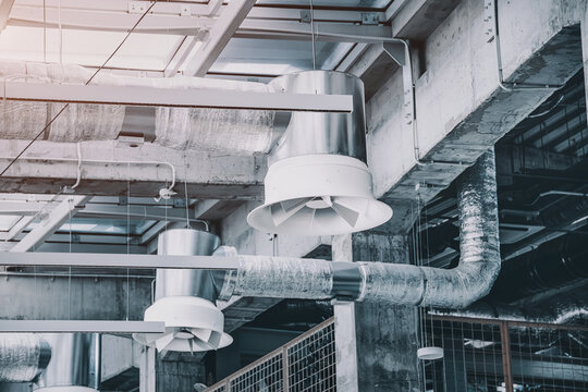 Industrial ventilation system with fan and insulated ductwork hanging from a modern building ceiling, ensuring air circulation and climate control